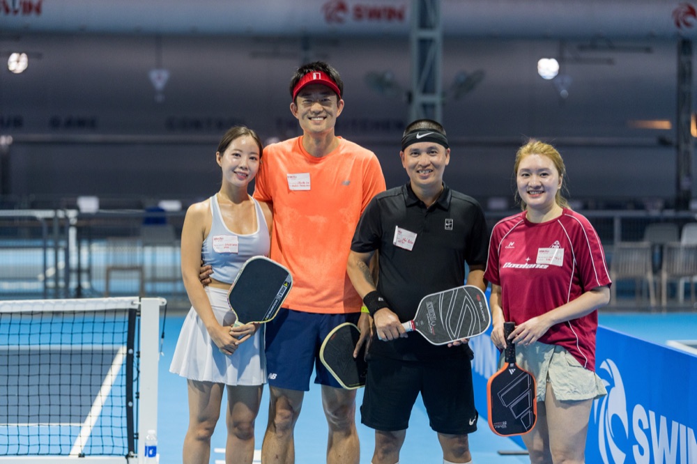 Four smiling pickleball players holding paddles on a blue court